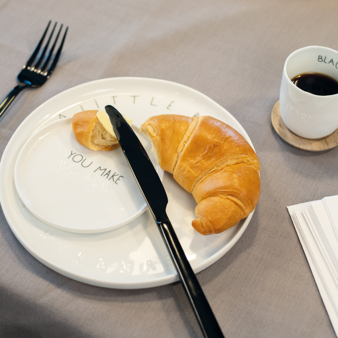 Ein weißer Teller mit einem Croissant und einem Messer darauf, elegant angerichtet. 