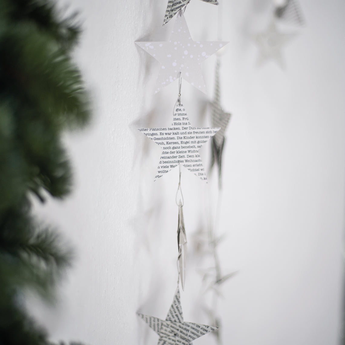 Ein weißer Weihnachtsbaum mit hängenden Papiersternen, der festliche Stimmung verbreitet.
