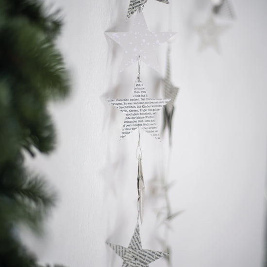 Ein weißer Weihnachtsbaum mit hängenden Papiersternen, der festliche Stimmung verbreitet.
